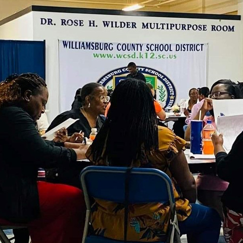 Group of black female educators sitting at a table in a multipurpose room in discussion with each other